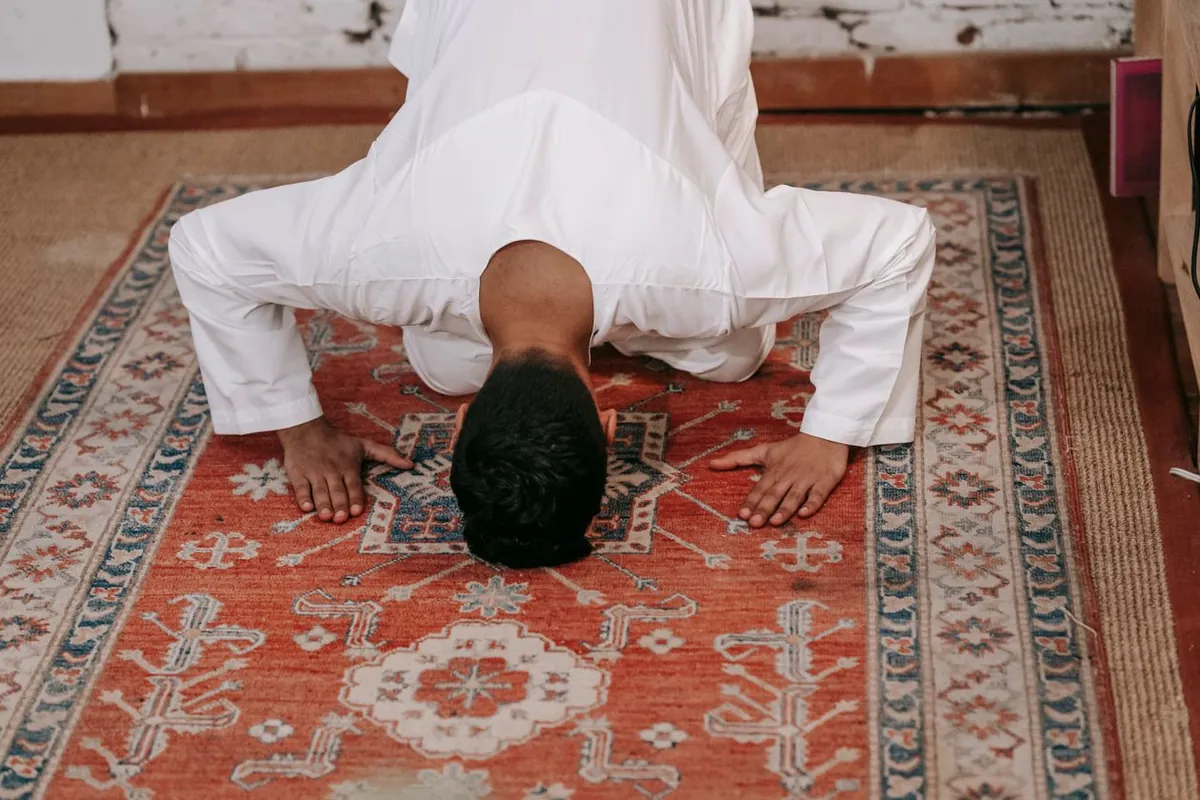 A man performing the prayer on a patterned prayer rug in a room, the way a beginner starts Tahajjud