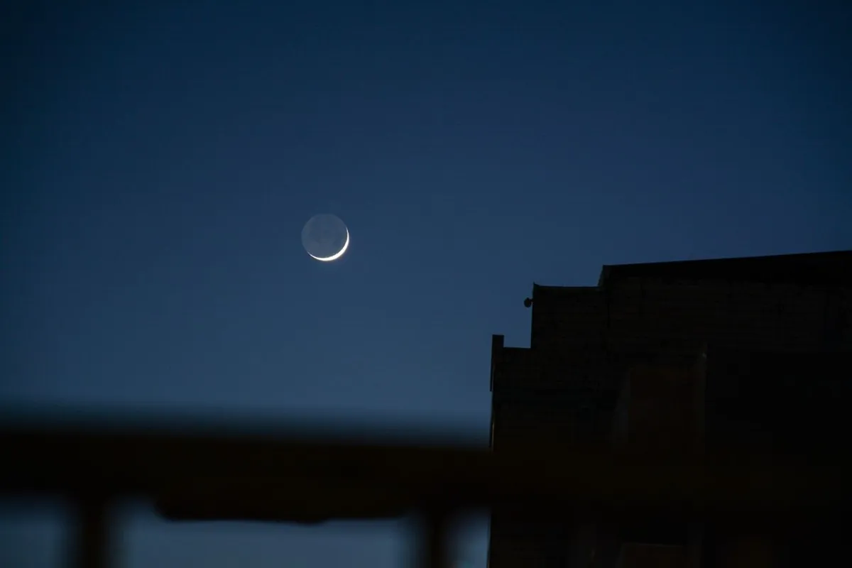 A crescent moon in a clear night sky above a silhouetted building