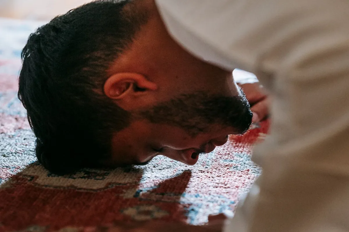 A worshipper bowing in prayer on a richly patterned prayer rug