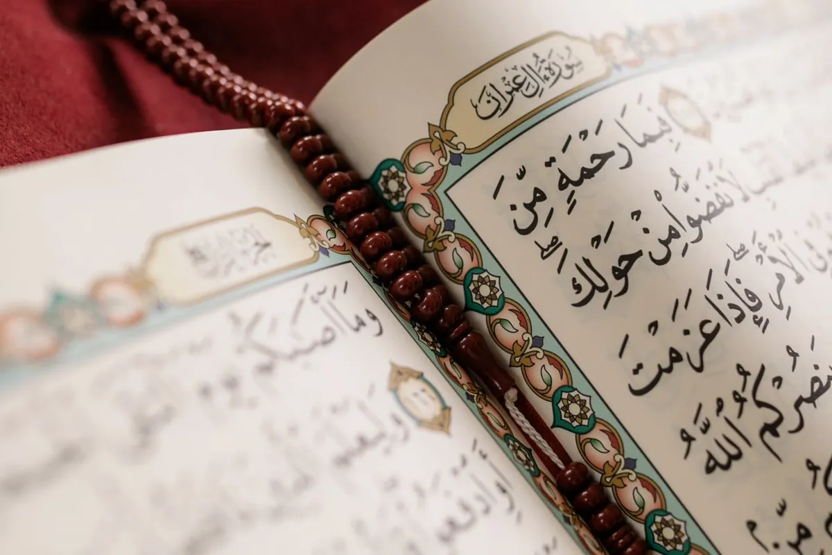An open Quran with a strand of prayer beads resting on its pages, in soft light