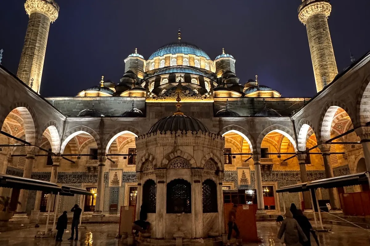 A grand mosque courtyard illuminated at night, its domes and minarets glowing against a deep blue sky
