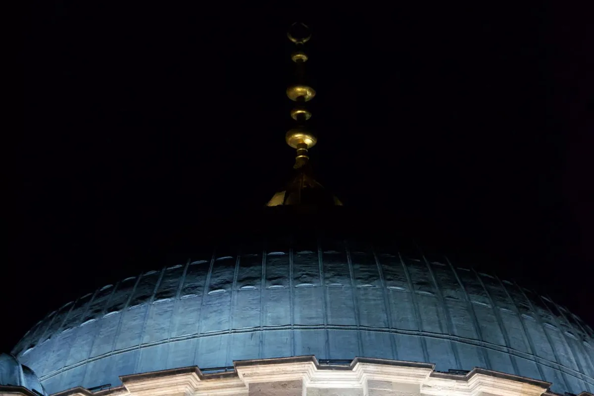 A mosque dome illuminated at night, glowing gold against a dark sky