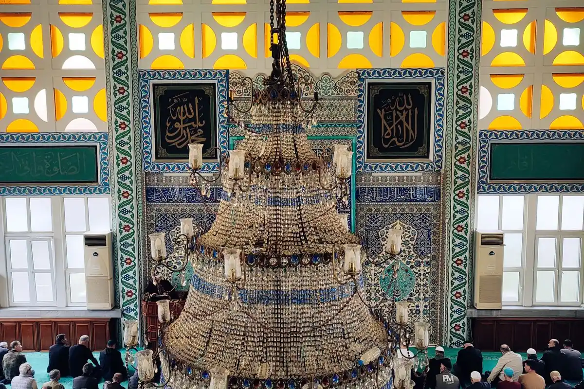 The interior of a mosque with a great chandelier, worshippers gathered in prayer below