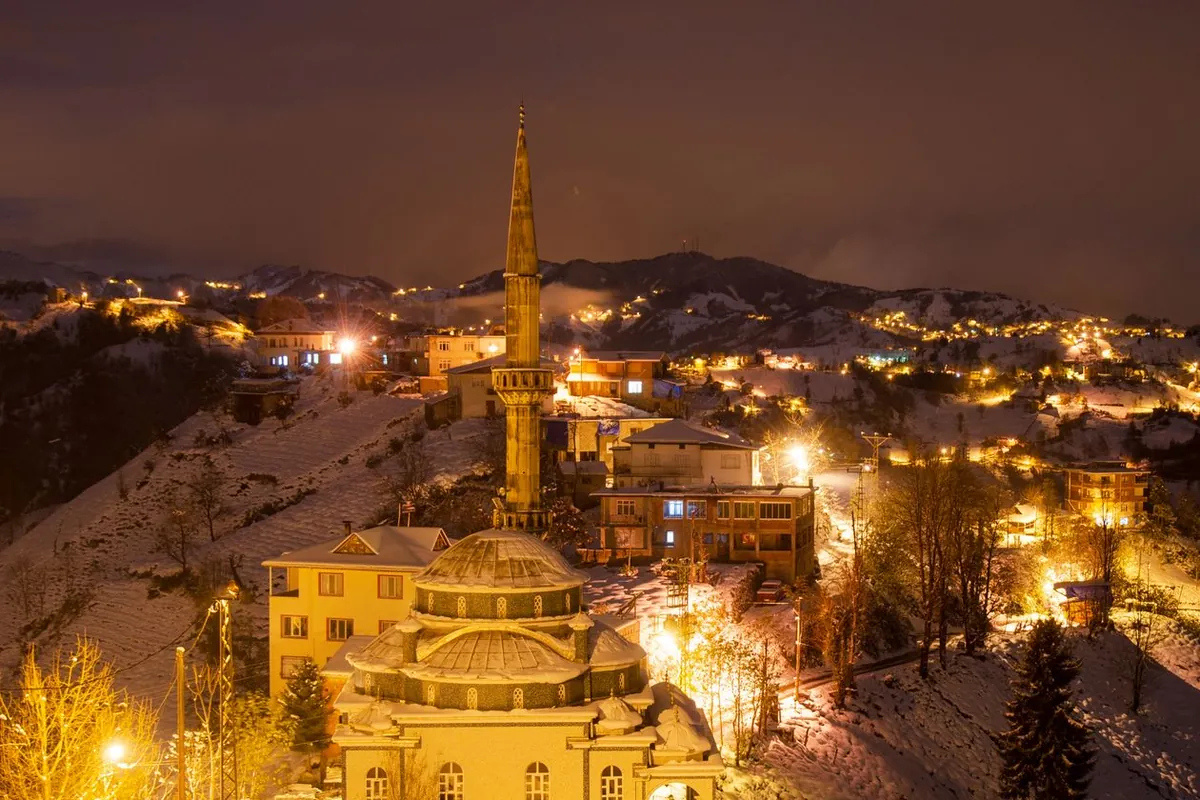 A mosque in a snow-covered village, illuminated against the winter night