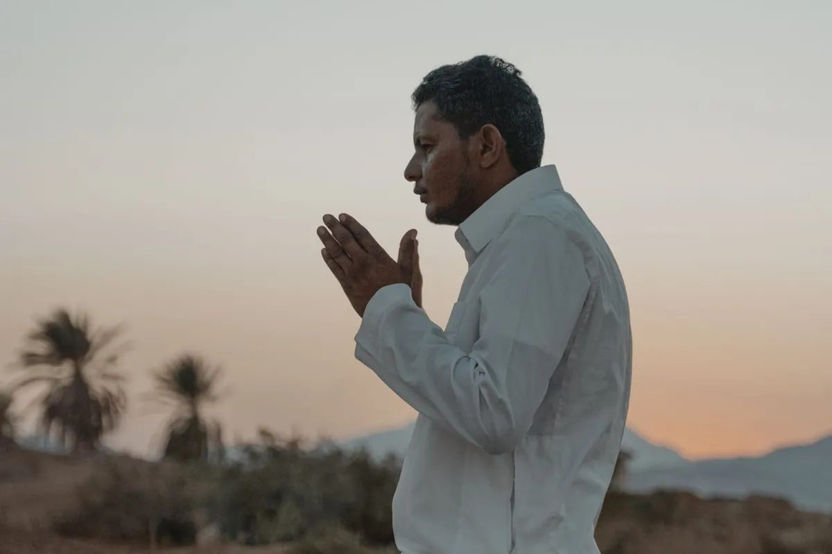 A man kneeling in prayer on a mat outdoors in the golden light of early morning